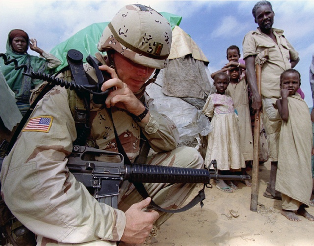 A U.S. soldier radios base, watched by displaced villagers, Mogadishu