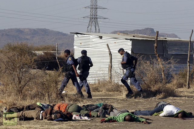 Policemen run in front of some of the dead miners after they were shot outside a South African mine in Rustenburg