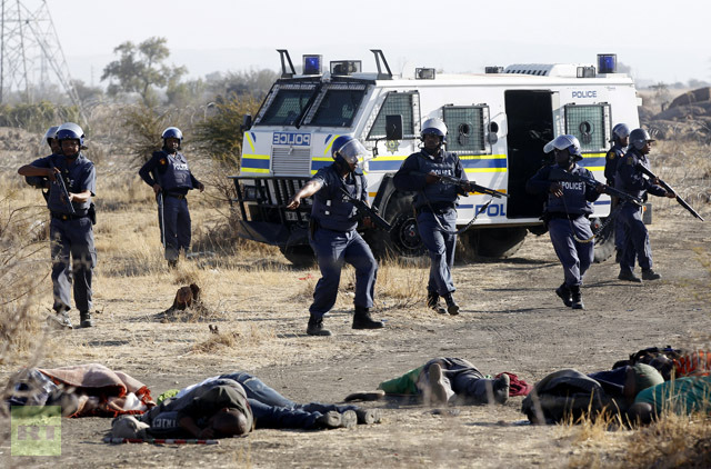 A policeman gestures in front of some of the dead miners after they were shot outside a South African mine in Rustenburg