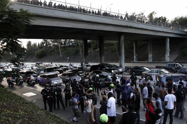 Demonstrators block traffic Sunday on the freeway in Los Angeles as police in riot gear stand at the ready.