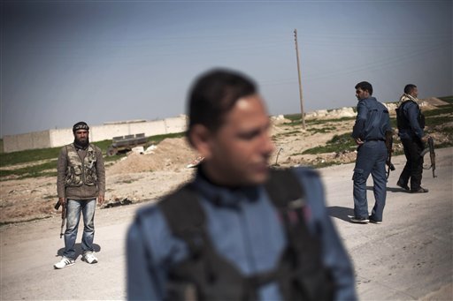 FILE - In this Wednesday, Feb. 27, 2013 file photo, members of the Kurdish Popular Protection Units and Free Syrian Army fighters stand guard at a check point at Ras al-Ayn, Syria.
