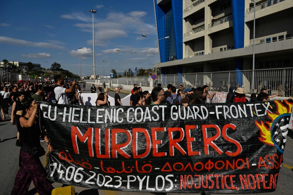 A protest banner reads,  "EU - Hellenic Coast Guard - Frontex Murderers. June 14, 2023, Pylos: No Justice, No Peace."